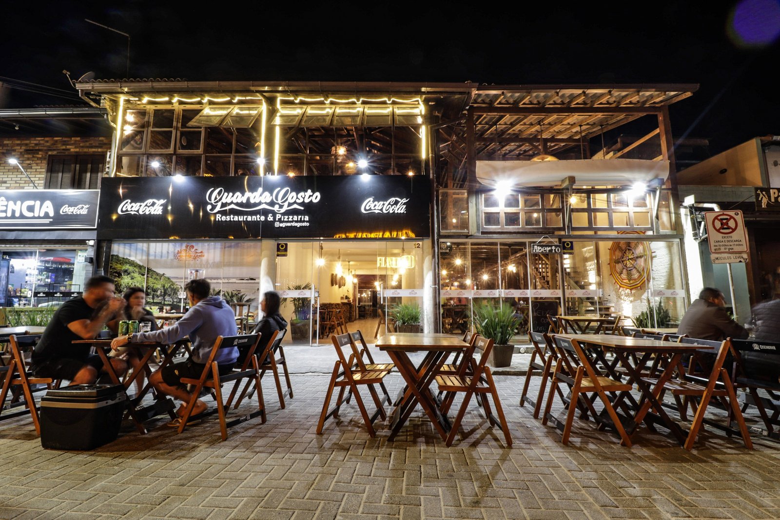 Entrada do Restaurante GuardaGosto com letreiro iluminado, estrutura de madeira e salão visível, na Guarda do Embaú (Palhoça/SC).